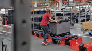 Une opératrice charge une remorque de train logistique avec un demi-trolley