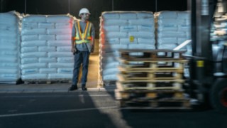 Être bien visible quand il le faut grâce à la veste de sécurité interactive Fenwick-Linde Un employé d’entrepôt et un chariot élévateur se croisent. Ce piéton est bien visible grâce à la veste de sécurité interactive Fenwick-Linde
