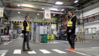 Deux collaborateurs se rencontrent dans l’entrepôt alors qu’ils portent la veste Linde Secure Distance Vest et le Linde Distance Beeper.