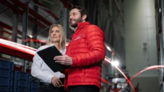 myFenwick s’adapte de manière flexible aux besoins de votre entreprise. Un homme en veste rouge Fenwick et une femme en chemise blanche se tiennent dans un grand entrepôt et regardent au loin.