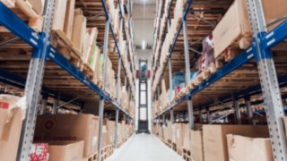 Un VNA soulève une palette dans un entrepôt à haut rayonnage, entouré de rayonnages garnis de cartons