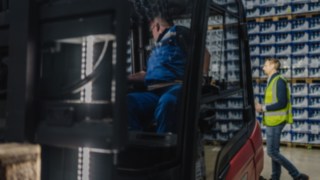 Un piéton portant un gilet de sécurité traverse l’entrepôt derrière un chariot élévateur.