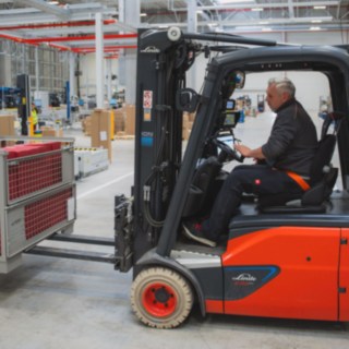 Un chariot électrique Fenwick transporte une caisse grillagée