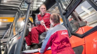 Nos collaborateurs jouent un rôle clé dans notre politique de développement durable. Une technicienne de service tend un outil à une autre technicienne de service dans le chariot élévateur.