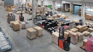 L’entrepôt logistique de Simon Hegele avec des employés qui trient et transportent des palettes de marchandises.
