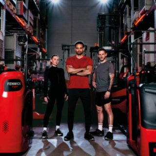 Une femme et deux hommes en tenue de sport se tiennent dans un entrepôt, au milieu de chariots de la marque Fenwick®.